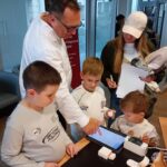 Dzieci pod nadzorem dorosłych tworzą rysunek na tablecie podczas warsztatów edukacyjnych.