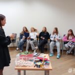 Uczestnicy warsztatów siedzą na krzesłach, a przed nimi stoi stół z materiałami plastycznymi.