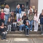 Grupa dziewcząt stoi i siedzi na schodach przed budynkiem.