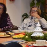 Uczestnicy Dyskusyjnego Klubu Książki siedzą przy stole nakrytym do herbaty, otoczeni świąteczną dekoracją.