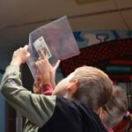 Dziecko trzyma plastikowe pudełko, wewnątrz którego znajduje się kartka papieru.