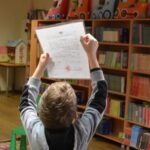 Chłopiec trzyma nad głową kartkę papieru, prawdopodobnie podczas zajęć edukacyjnych.