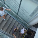 Młodzi ludzie wchodzą po schodach w nowoczesnym budynku z szklanymi przeszkleniami.