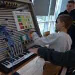 Chłopiec gra na klawiaturze podłączonej do urządzenia edukacyjnego z tablicą kolorów.