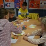 Dzieci siedzą przy stole, tworząc konstrukcje z koralików i innych materiałów.