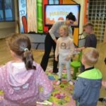 Dziecko stoi przed ekranem, a dorosły wskazuje mu coś podczas zajęć edukacyjnych.