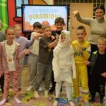 Grupa dzieci w strojach, imitujących mumie, pozuje do zdjęcia przed ekranem z napisem "piramida".