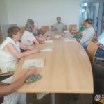 Grupa osób siedzi przy długim stole w sali spotkań, prawdopodobnie podczas dyskusji o historii i kulturze mniejszości narodowych.