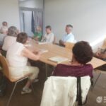 Grupa osób siedzi przy stole podczas spotkania w bibliotece, prawdopodobnie omawiając historię i sytuację mniejszości narodowych.