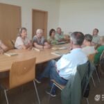 Grupa osób siedzi przy okrągłym stole podczas spotkania w bibliotece, prawdopodobnie omawiając historię i sytuację mniejszości narodowych.