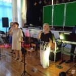 Dwóch śpiewaków stoi przed mikrofonami na scenie podczas występu zespołu Piosenki Odkopanej.