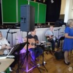 Na scenie zespół muzyczny wykonuje utwory podczas koncertu z mikrofonami i głośnikami w tle.