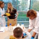 Uczniowie pod nadzorem prowadzącego eksperymentują z odczynnikami chemicznymi podczas warsztatów w laboratorium.