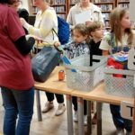 Uczestnicy wydarzenia ustawiają się do stanowiska z materiałami edukacyjnymi w bibliotece miejskiej.
