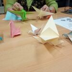 Na stole leżą kolorowe papierowe żurawie wykonane techniką origami.