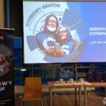 Na projekcji prezentacji widnieje logo programu "Cyfrowy Senior" przedstawiające stylizowanych Indian z tabletami i hasłem związanym z bezpieczeństwem cyfrowym.