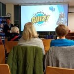Na ekranie wyświetlony napis "QUIZ!" podczas spotkania edukacyjnego dla seniorów.