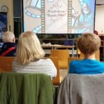 Na ekranie wyświetlana jest prezentacja dotycząca oszustw internetowych, a przed nią siedzą słuchacze.