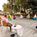 Uczestnicy zajęć z jogi siedzą na krzesłach w otoczeniu drzew w bibliotece publicznej.