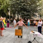 Uczestnicy zajęć jogi wykonują ćwiczenia na zewnątrz, w pobliżu budynku biblioteki.