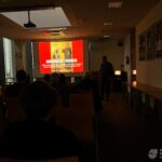 Na ekranie wyświetlana jest prezentacja dotycząca symboliki regaliów koronacyjnych, a przed ekranem siedzą słuchacze wykładu.