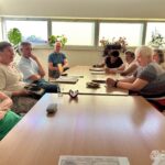 Grupa osób siedzi przy stole podczas spotkania w bibliotece, prawdopodobnie dyskutując o historii i sytuacji mniejszości narodowych.