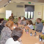 Uczestniczki warsztatów tworzą biżuterię z żywicy epoksydowej przy długim stole w jasnym pomieszczeniu.