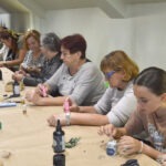 Kobiety siedzą przy stole, tworząc biżuterię z żywicy epoksydowej podczas warsztatów rękodzielniczych.