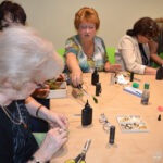 Kobiety siedzą przy stole, wykonując prace rękodzielnicze z wykorzystaniem żywicy epoksydowej i narzędzi.