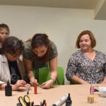 Uczestnicy warsztatów z żywicy epoksydowej skupiają się nad tworzeniem biżuterii przy wspólnym stole.