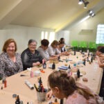 Uczestniczki warsztatów tworzą biżuterię z żywicy epoksydowej przy długim stole pokrytym materiałami do pracy.