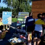 Na pikniku edukacyjnym ustawiono stoisko z plakatami informacyjnymi oraz półki z książkami i roślinami.