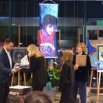 Wystawa „Pierwszy krok” prezentuje portret inspirowany zespołem The Beatles, zawieszony obok stojaków z pracami artystycznymi.