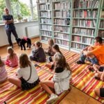 Grupa dzieci słucha prezentera z psem podczas zajęć w bibliotece.