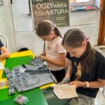 Dzieci podczas warsztatów plastycznych, wykorzystując papier i inne materiały.