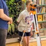 Dziewczynka używa dalmierza zamontowanego na statywie podczas zajęć edukacyjnych w bibliotece.