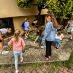 Grupa dzieci podczas zajęć plastycznych na świeżym powietrzu, prawdopodobnie w ramach programu "Kulturalne Wakacje".