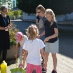 Grupa dzieci i dorosłych uczestniczy w warsztatach edukacyjnych nad brzegiem rzeki.