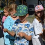 Dzieci obserwują coś trzymanego w dłoni podczas pikniku edukacyjnego.