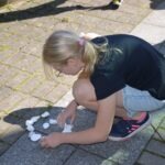 Dziecko układa z kamieni kształt koła na chodniku podczas pikniku edukacyjnego.