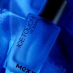 Butelka perfum Ice Touch Woman marki Mexx owinięta w niebieski papier, oświetlona intensywnym błękitem.