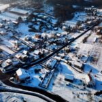 Widok lotniczy na pokrytą śniegiem wieś z drewnianymi domami i zabudowaniami gospodarczymi.