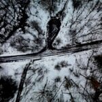 Widok z góry na kręty, ośnieżony leśny trakt otoczony nagimi drzewami.