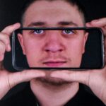 Mężczyzna trzyma telefon przed twarzą, kadrując swoje oczy.