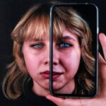 Portret dziewczyny z telefonem w ręce, na którym widoczny jest jej odbicie, tworząc wrażenie podwójnej twarzy.