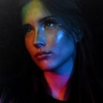 Portret młodej kobiety o ciemnych włosach, oświetlonej kolorowymi światłami.