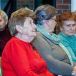 Słuchacze koncertu siedzą blisko siebie, skupieni na występie zespołu.