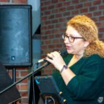 Wokalistka zespołu trzyma mikrofon podczas występu na scenie w bibliotece.