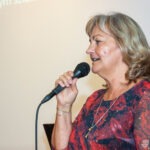 Kobieta trzyma mikrofon i śpiewa, uśmiechając się do publiczności.