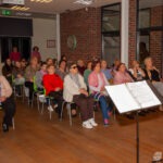 Publiczność siedzi na krzesłach, słuchając koncertu zespołu w bibliotece.